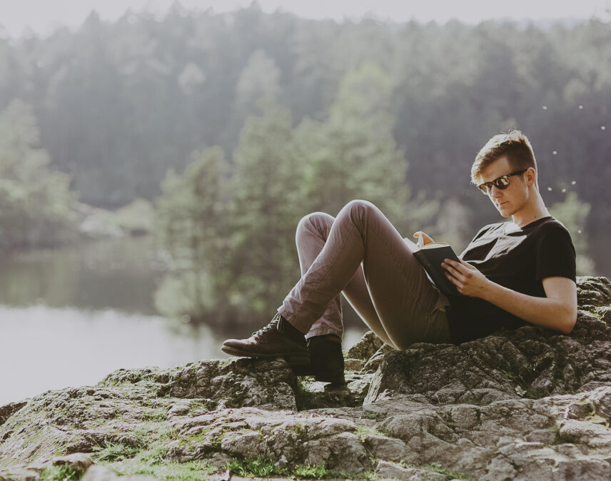 Person reclining on a rocky lakeside in View Royal, near Victoria, BC, reading a book amidst a serene natural environment with lush greenery and calm waters