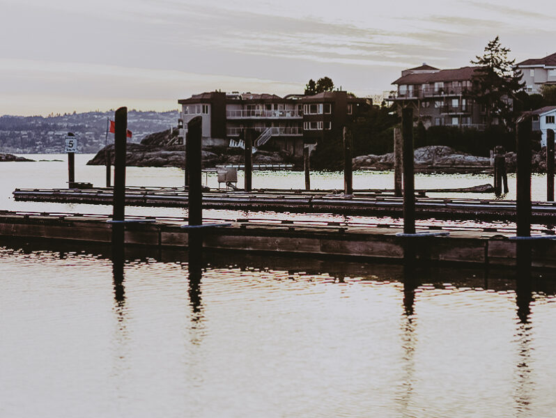 A tranquil marina in Esquimalt during sunset, featuring calm waters, mooring docks, and nearby waterfront residences, highlighting properties managed by Clover Residential in Victoria, BC