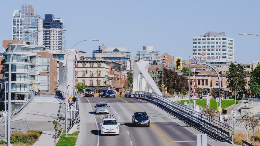 Downtown cityscape view featuring cars and cyclists crossing a modern bridge, surrounded by high-rise buildings and green spaces