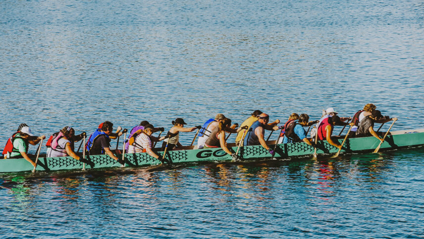 Group of people paddling a dragon boat on a calm blue body of water during a sunny day