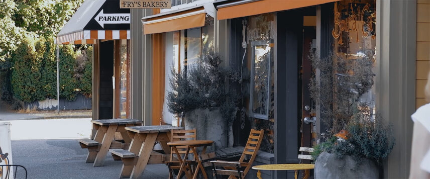 Charming street view of Fry's Bakery featuring outdoor wooden tables, colorful awnings, and potted greenery along a cozy sidewalk setting