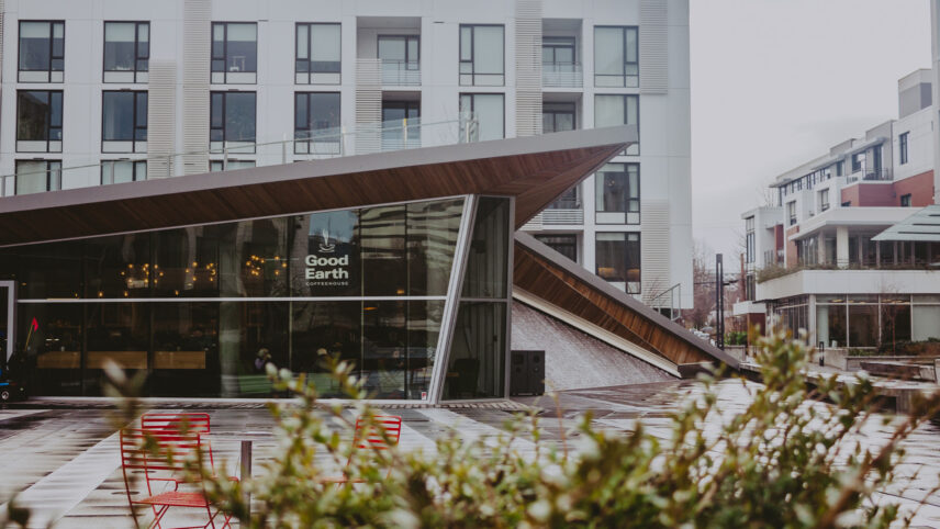 Modern exterior of Good Earth Coffeehouse featuring sleek architecture with large glass windows, surrounded by a contemporary urban plaza with red chairs and greenery