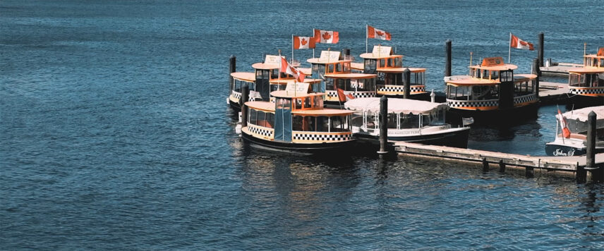 Harbour scene with charming water taxis adorned with Canadian flags docked at the marina, surrounded by calm blue waters in downtown Victoria, BC