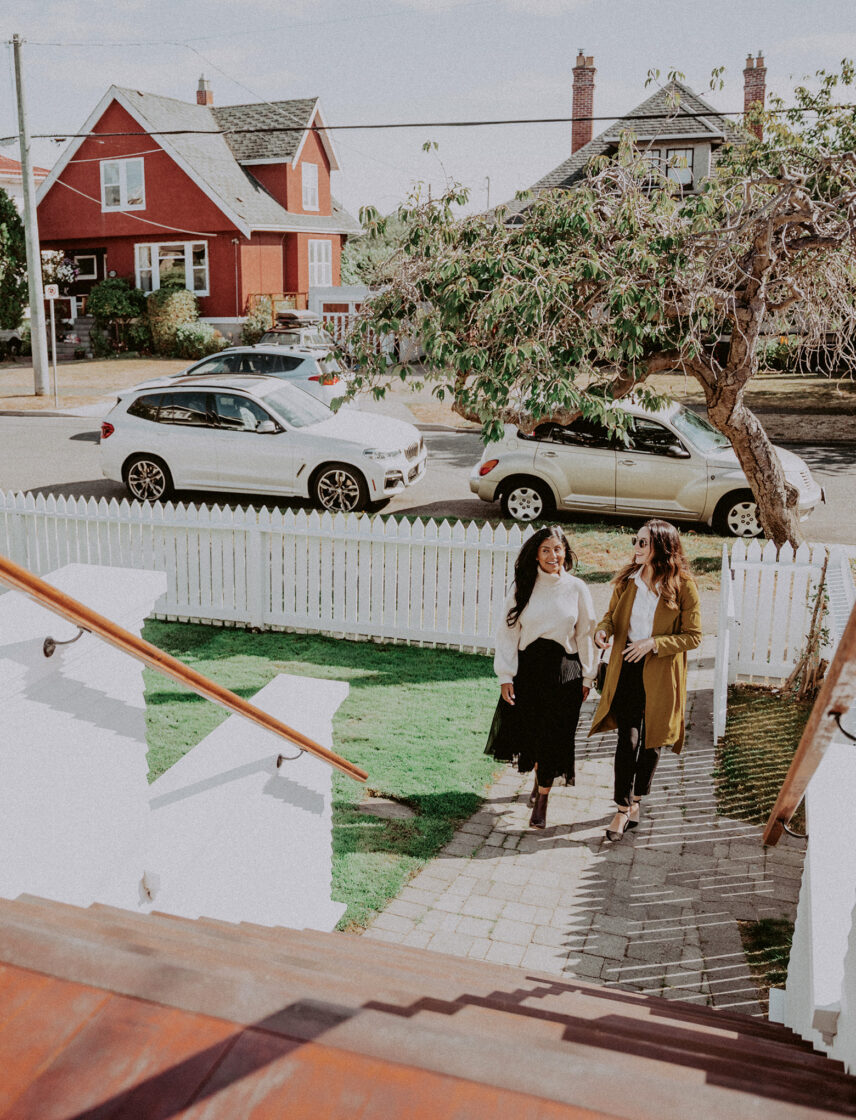 Hannah Hayworth and a colleague walking up a charming pathway towards a classic white picket-fenced home in Victoria, BC, symbolizing personalized real estate service and community connections