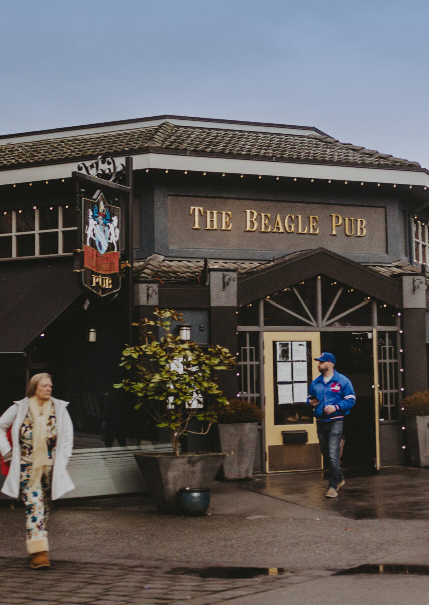 Exterior of The Beagle Pub featuring a dark facade, gold lettering, and decorative signage, with patrons walking outside on a cloudy day