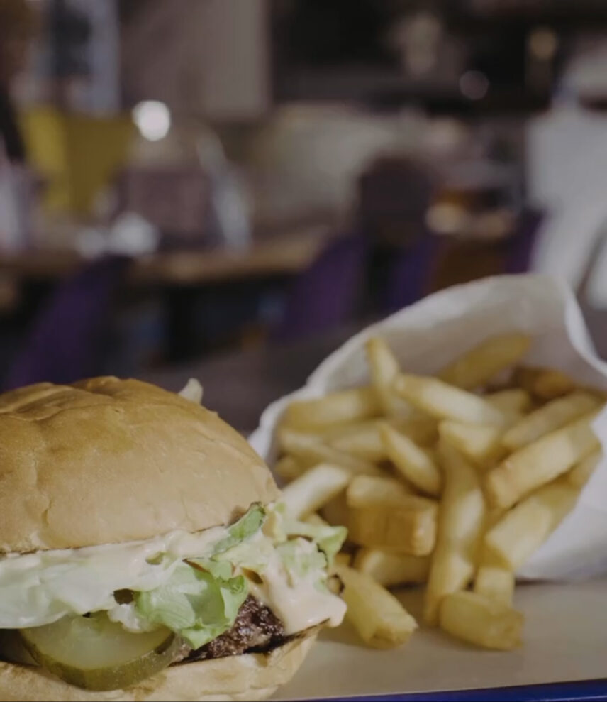 Close-up of a burger with lettuce, pickles, and sauce, served alongside crispy fries in a paper bag