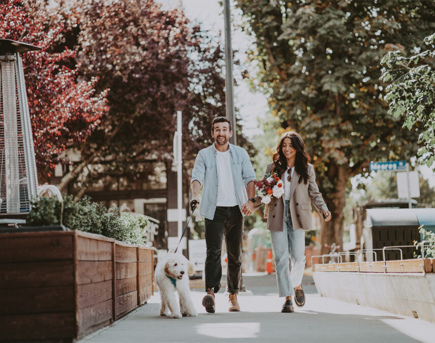 Couple strolling through a lively neighborhood with their dog, near a rental property managed by Clover Residential in Victoria, BC