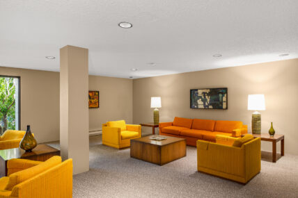 Common area at 1433 Faircliff Lane listed by Clover Residential in Victoria, BC, showcasing retro yellow and orange furniture, modern artwork, and warm ambient lighting