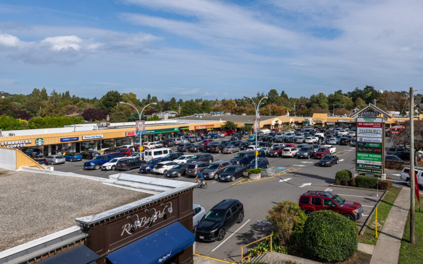 A busy shopping center parking lot at Fairfield Plaza located at 624 Cornwall Street, Victoria, BC, featuring various storefronts including Starbucks and BC Liquor Store, managed by Folio Group at Clover Residential in Victoria, BC