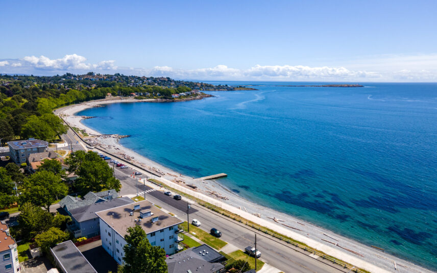 Aerial view of a scenic waterfront property near 624 Cornwall Street, Victoria, BC, featuring a clear blue shoreline, residential buildings, and lush greenery, managed by Folio Group at Clover Residential in Victoria, BC
