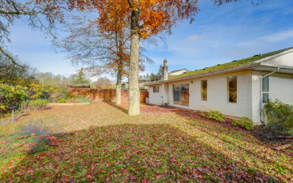 The backyard of the property at 1293 Layritz Place, managed by Clover Residential in Victoria, BC. The yard features a vibrant autumn setting with fallen leaves, mature trees, and a wooden fence enclosing the area.