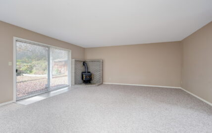 Living room featuring a cozy wood-burning stove, carpeted flooring, and sliding glass doors leading to the backyard at 1293 Layritz Place, managed by Clover Residential in Victoria, BC