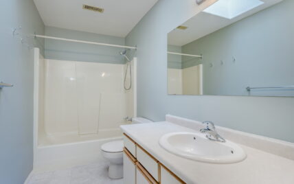 Bright bathroom with light blue walls, a large mirror, white countertop, and a combined bathtub and shower at 1293 Layritz Place, managed by Clover Residential in Victoria, BC.