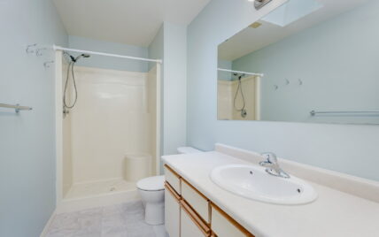 This is a clean and functional bathroom featuring a spacious shower with light blue walls and simple white fixtures, located at 1293 Layritz Place, managed by Clover Residential in Victoria, BC.