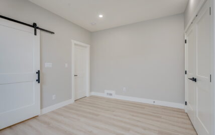 Bedroom with a modern barn-style sliding door, light wood laminate flooring, and recessed lighting at 337 Robertson Street, managed by Clover Residential in Victoria, BC