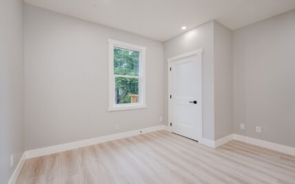 Bedroom with light wood laminate flooring, recessed lighting, and a large window overlooking greenery at 337 Robertson Street, managed by Clover Residential in Victoria, BC