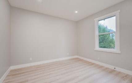 Bedroom featuring light wood laminate flooring, recessed lighting, and a large window with views of greenery at 337 Robertson Street, managed by Clover Residential in Victoria, BC