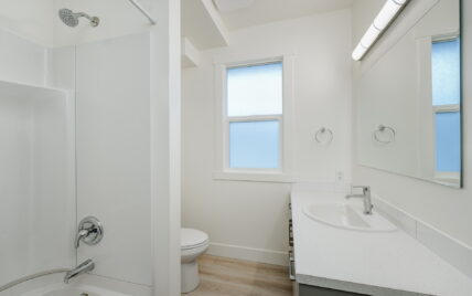 Modern bathroom with a full bathtub and shower combination, quartz countertop vanity, large mirror, and frosted window at 337 Robertson Street, managed by Clover Residential in Victoria, BC