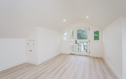 Bright attic room with vaulted ceilings, light wood laminate flooring, and French doors leading to a small balcony at 337 Robertson Street, managed by Clover Residential in Victoria, BC