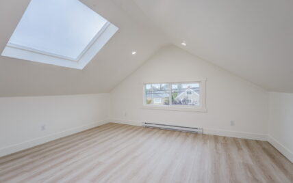 Bright attic room with vaulted ceilings, a skylight, recessed lighting, and a large window offering views of the neighborhood at 337 Robertson Street, managed by Clover Residential in Victoria, BC