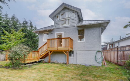 Exterior view of the rear of the home featuring a wooden deck with stairs, fenced backyard, and upper-level balcony at 337 Robertson Street, managed by Clover Residential in Victoria, BC