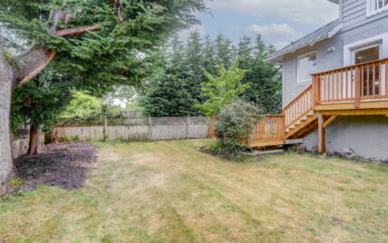 Spacious fenced backyard with mature trees, greenery, and a wooden deck with stairs at 337 Robertson Street, managed by Clover Residential in Victoria, BC