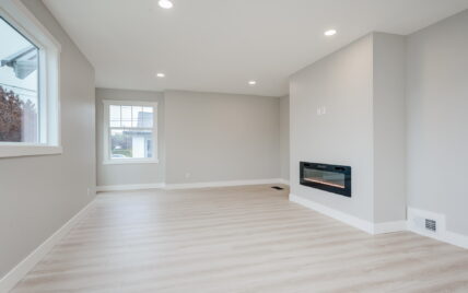 Living room with modern electric fireplace and natural light from large windows, featuring light wood laminate flooring at 337 Robertson Street, managed by Clover Residential in Victoria, BC