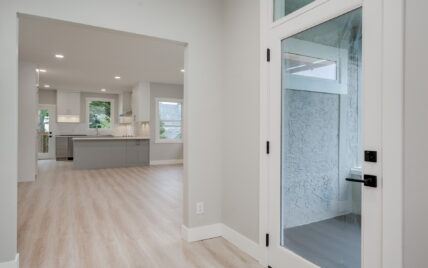 Entryway view leading to a modern kitchen with sleek cabinetry, a central island, and light wood laminate flooring at 337 Robertson Street, managed by Clover Residential in Victoria, BC