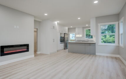 Open concept living space featuring a modern electric fireplace, a sleek kitchen with white cabinetry, stainless steel appliances, and a large island at 337 Robertson Street, managed by Clover Residential in Victoria, BC